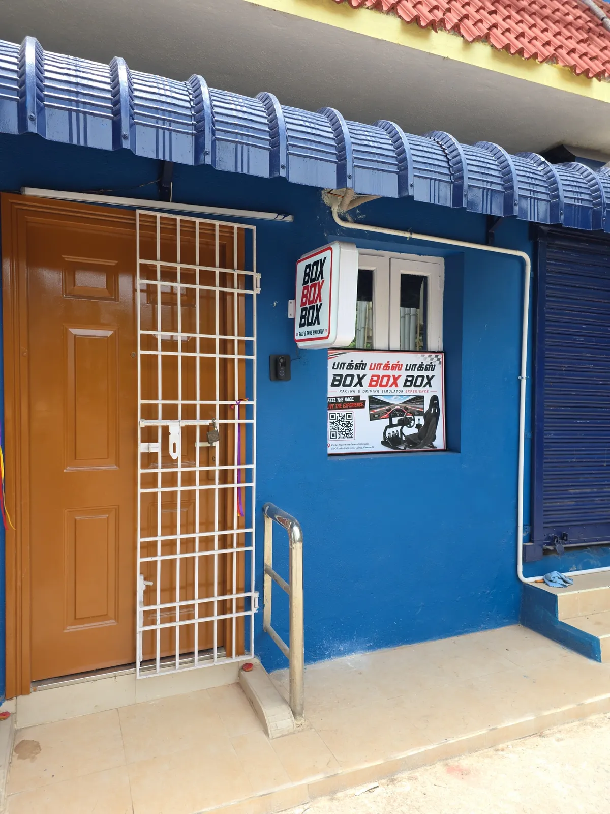 The entrance to BoxBoxBox in the Readymade Garments Complex, SIDCO Industrial Estate, Guindy — a blue unit with a lit BOX BOX BOX sign over the door and a Tamil and English banner beside it.
