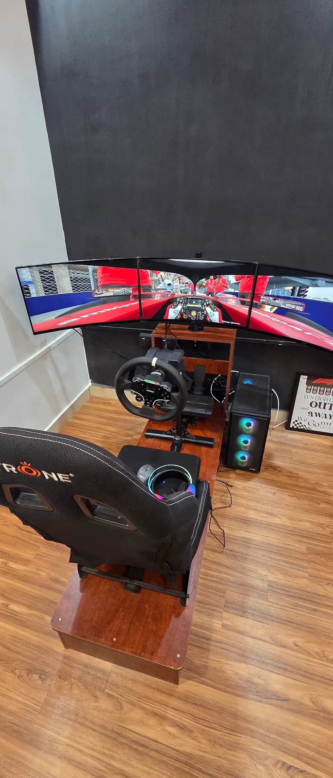 The PODIUM rig at BoxBoxBox Guindy — a MOZA direct-drive wheel and racing seat on a wooden platform, facing three curved screens running an F1 car down the pit straight.