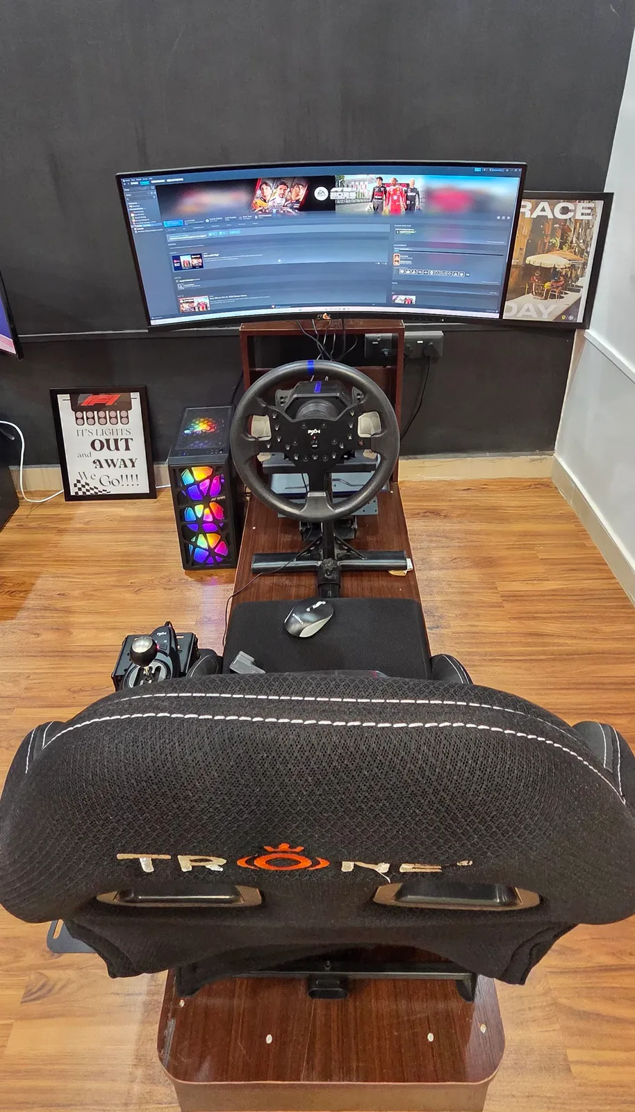 The ROOKIE rig at BoxBoxBox Guindy — a PXN wheel and a TRONE racing seat facing one big curved screen, with the H-pattern gearstick mounted at the driver's left hand.